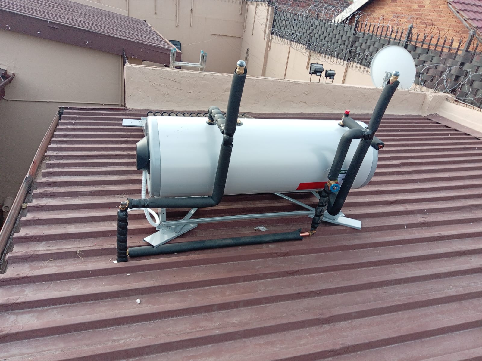 Solar geyser tank mounted on corrugated roof with insulated pipes