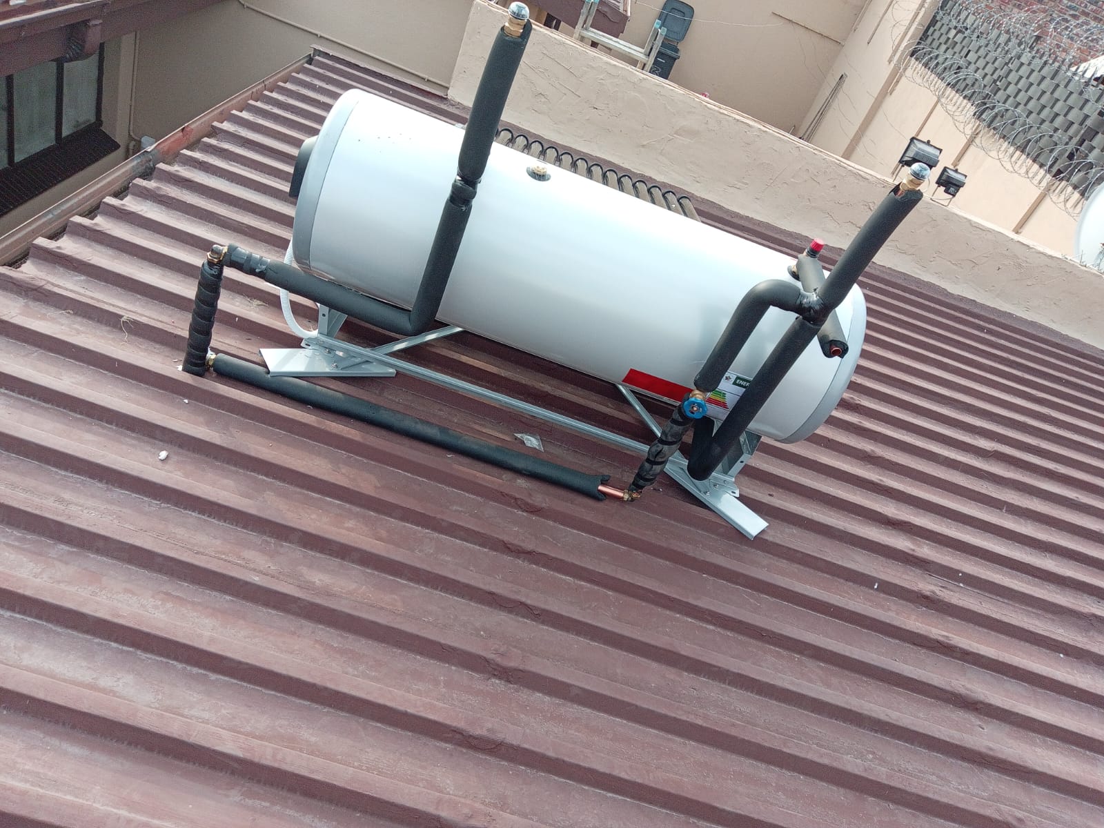 Solar geyser tank installation with pipe connections on metal roof