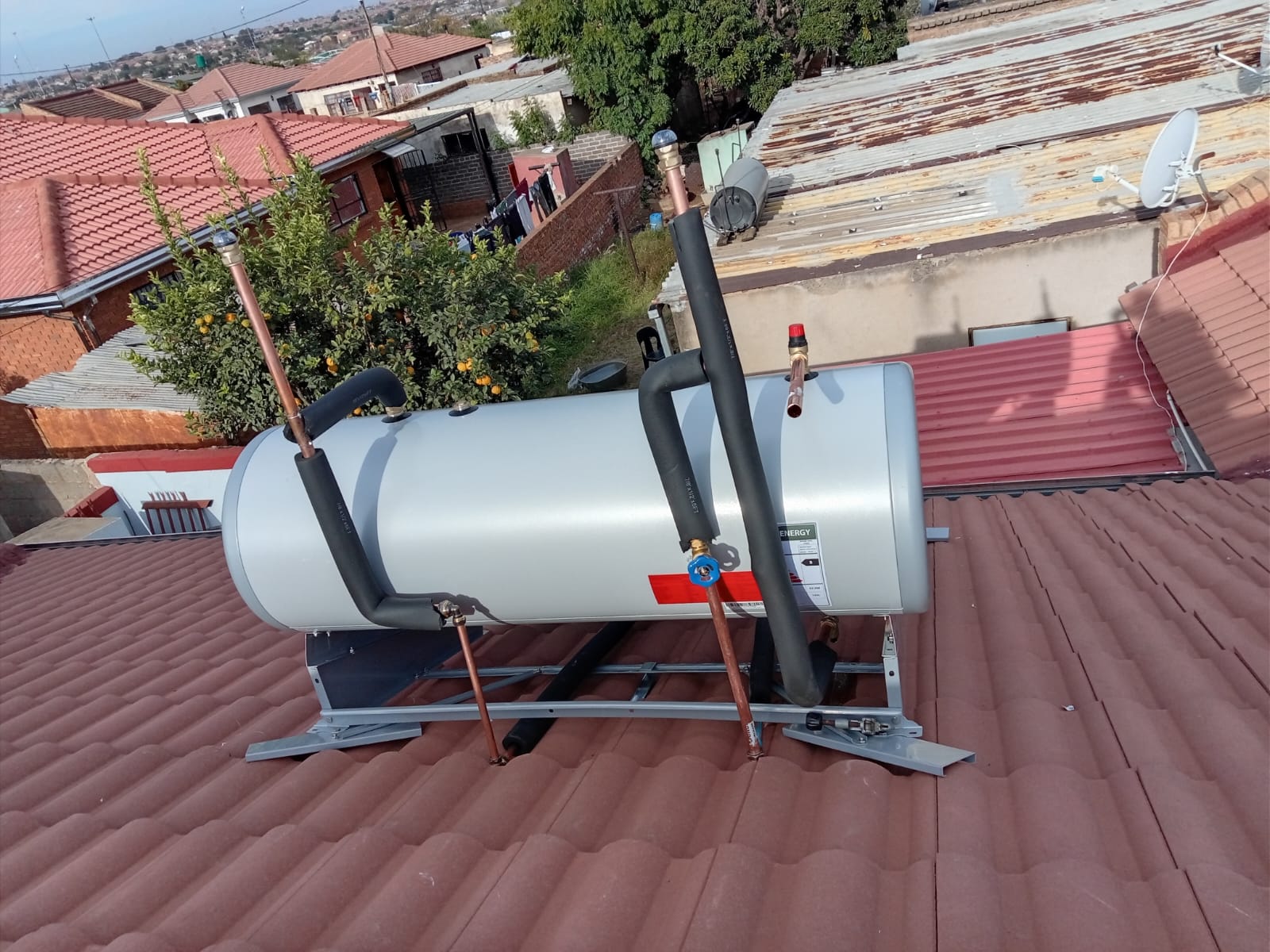 Solar geyser tank with copper pipes and valves on tiled roof