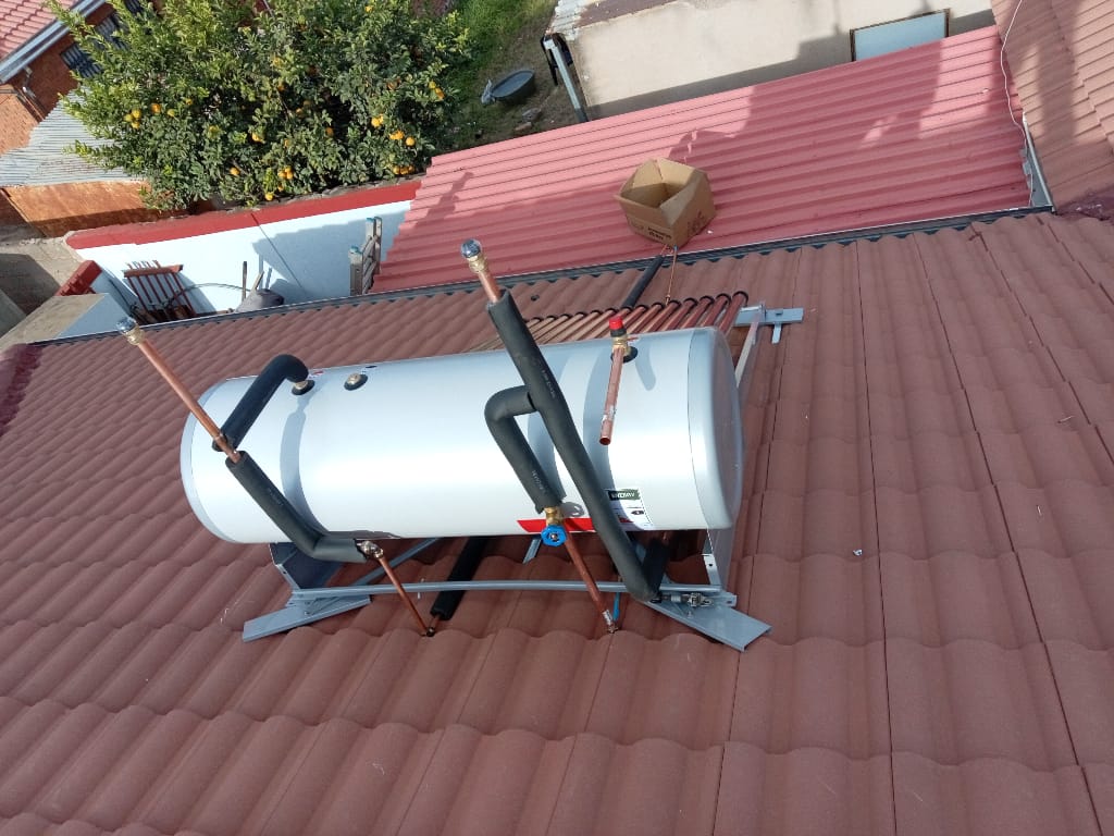 Solar geyser tank top view with pipe connections on tiled roof