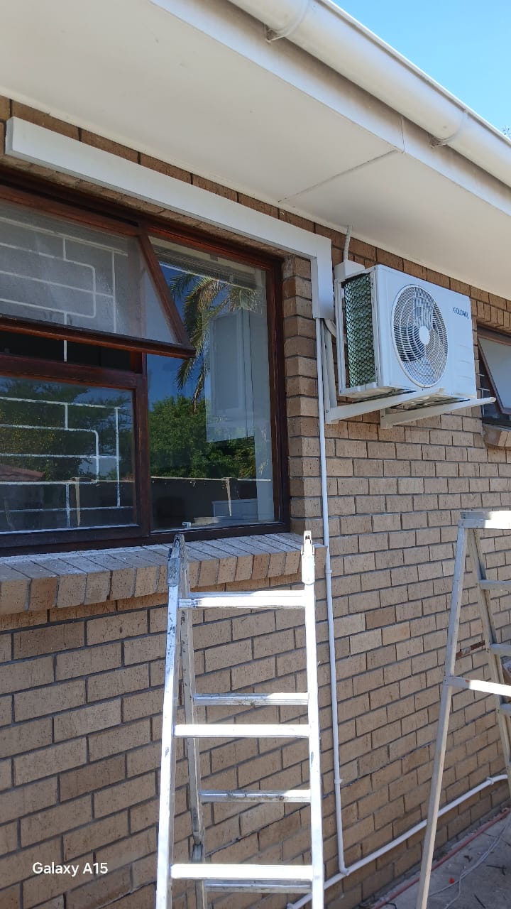Goldair AC outdoor unit on brick wall with ladder during installation