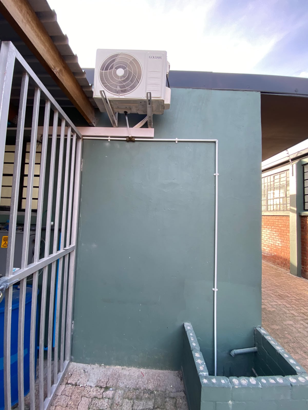 Goldair AC outdoor unit with neat pipe trunking on green wall