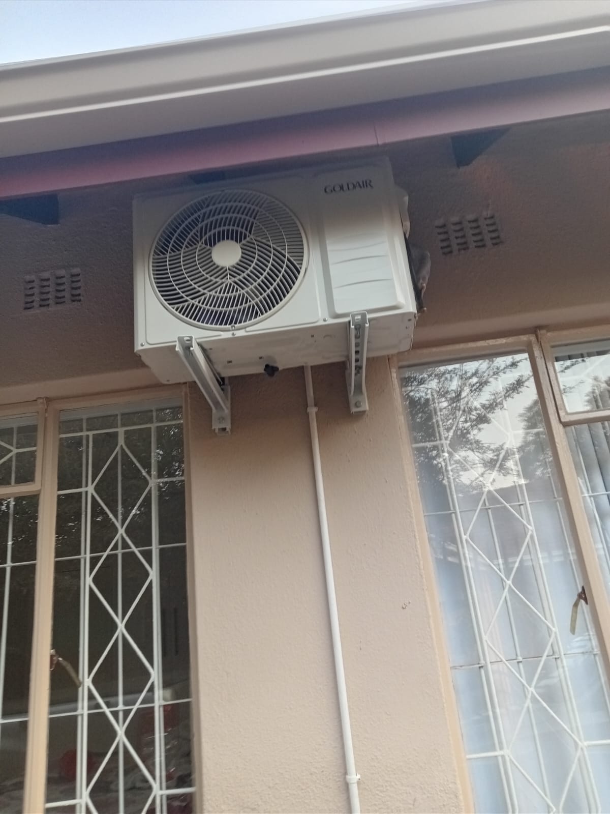 Goldair AC outdoor unit on wall bracket between windows under eaves